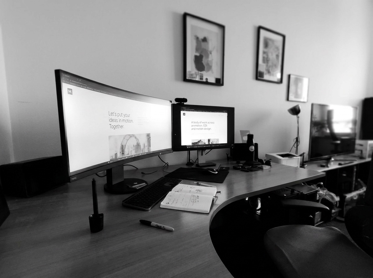 Creative workspace with dual monitors and a sketchbook